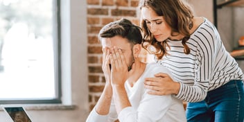 standing woman hugs seated distressed man  
