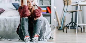 teenage girl looking unhappy sitting on her bedroom floor