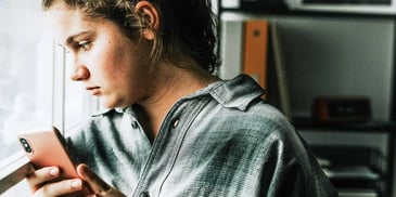 teen girl sitting alone by window who looks unhappy