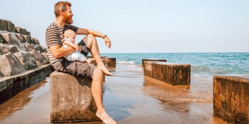 man and infant sitting together on the beach