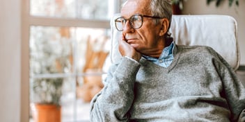 older man looking out window with chin in hands
