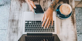 hands typing on laptop and holding phone