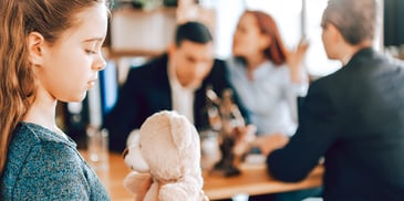 child holding teddy bear near arguing adults