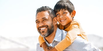 man with beard holding child on back near mountains