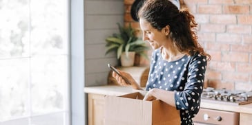 woman standing in kitchen with phone and moving box