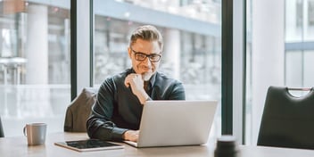 man sitting at laptop in front of big city window