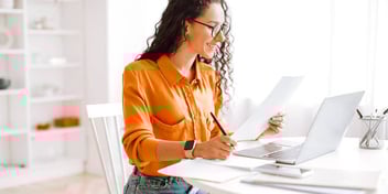 Woman looking at computer holding papers