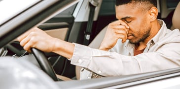 man sitting behind wheel of car with face in hand