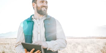 man holding book smiling field and mountain sun