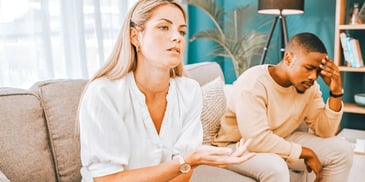 couple sits on couch frustrated with each other