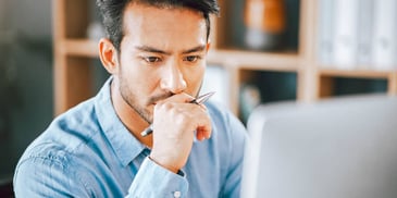thoughtful frowning man at computer with pen in hand