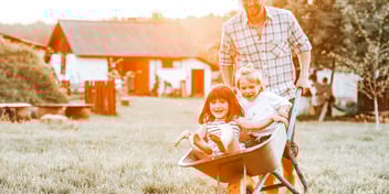 dad pushing two little kids in wheelbarrow 