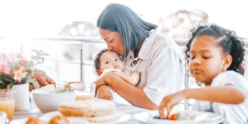 mom kissing baby and sitting with toddler