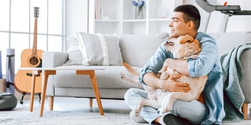 man sitting quietly in sunny room while hugging dog 