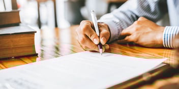 hand signing paper with pen on wooden desk