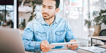 man sitting at computer next to window and green plants