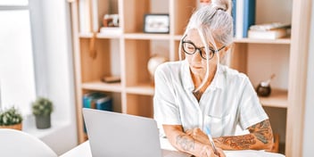 woman sitting at laptop in front of bookcase and near window