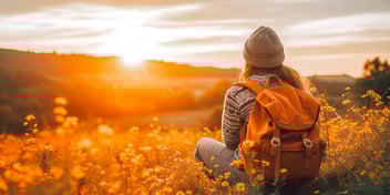 woman with backpack sitting in field looking at mountain with sunrise