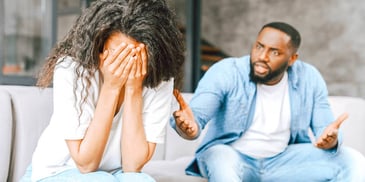 angry man arguing with his wife who is burying her face in her hands in frustration