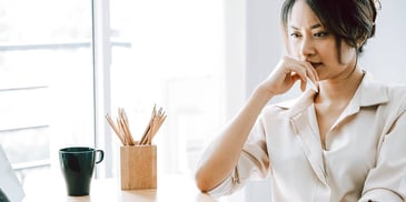 Young Asian woman sitting at her desk contemplating