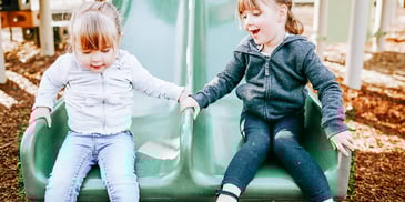 two young sisters play together on a slide at the park