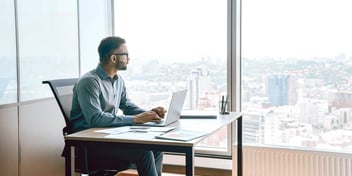man looking out his office window at a city view