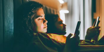 couple in bed together but on their phones ignoring each other