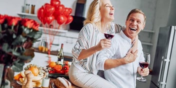 Couple in the kitchen together smiling with wine in hand
