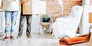 two people standing in a messy room with boxes and personal property