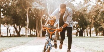 dad teaching son how to ride a bike