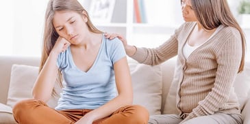preteen girl being comforted by her mother as they sit and talk on the couch