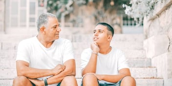 father and son sitting on a staircase outdoors and talking about life