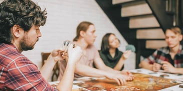 man holding cards sitting away from his friends and feeling excluded