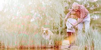 grandfather and grandson fishing at a pond with their dog watching on shore