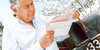 grumpy looking older man taking mail out of his mailbox