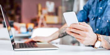 man checking his phone while working on laptop