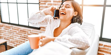woman laughing and talking on her phone while she sips a cup of coffee