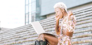 woman raising her arms in relief while looking at her laptop and sitting on courthouse steps