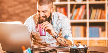 man drinking coffee while reading on his laptop