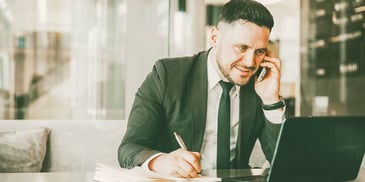 man talking on the phone and taking notes while looking at his computer monitor