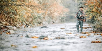 man standing in a river fishing with a fly rod
