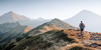 man with hiking poles scaling a scenic mountain
