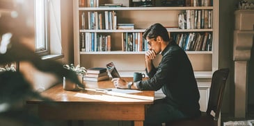 man reading on his laptop in front of book shelf