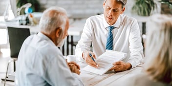 A man in business attire is reviewing a document with an older couple