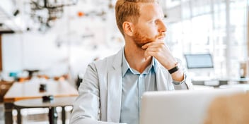 man sitting in front of laptop looking out the window at a cafe 