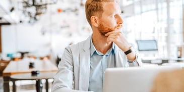 man sitting in front of laptop looking out the window at a cafe 
