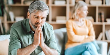 man deep in thought sitting apart from his wife on their couch