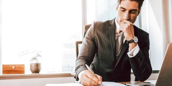 Man wearing a business suite taking notes in his office