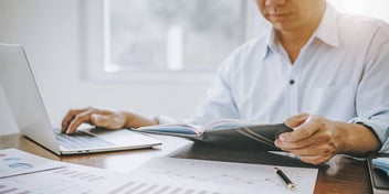 man looking at laptop and notebook on desk