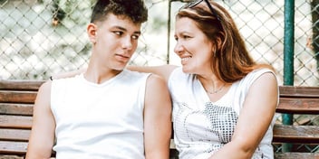 A mother and son sitting on a bench together looking at one another